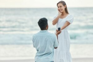 Amour, plage et demande en mariage, un couple avec une bague de fiançailles au bord de l'océan. Elle a dit oui, femme et homme