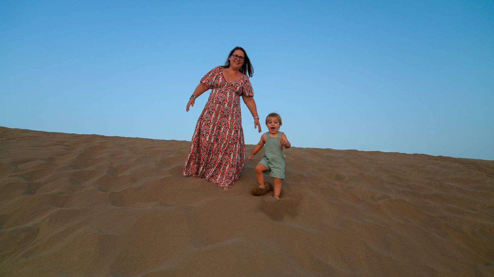 Mother jumping and running with toddler on the dunes Gran Canaria
