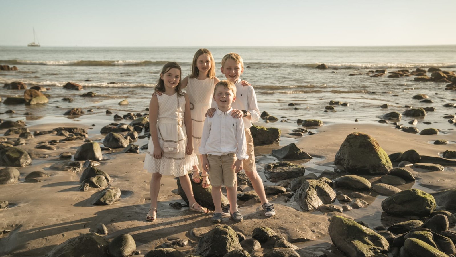 Four children arm in arm on rocky beach at sunset Gran Canaria