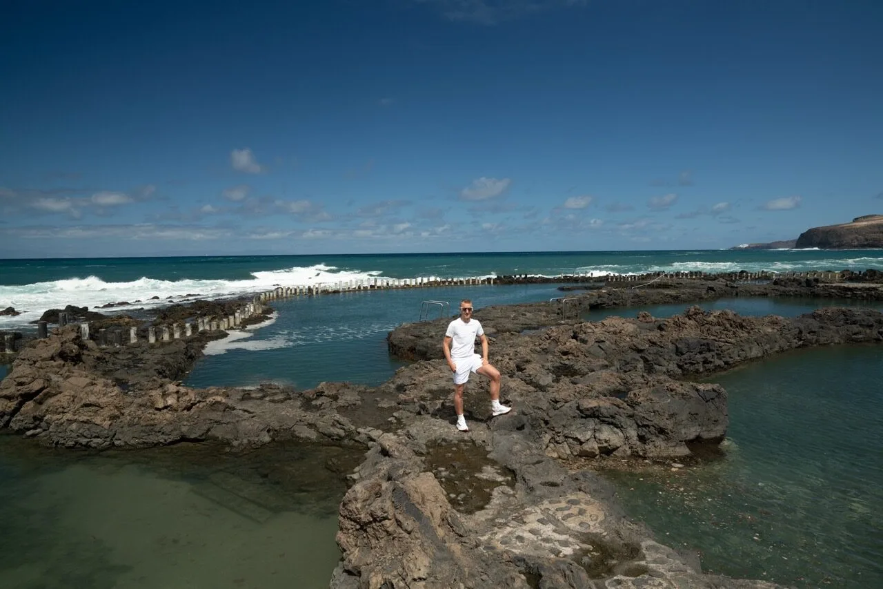 Man in white standing on volcanic rocks natural pools Agaete Gran Canaria blue sky ocean