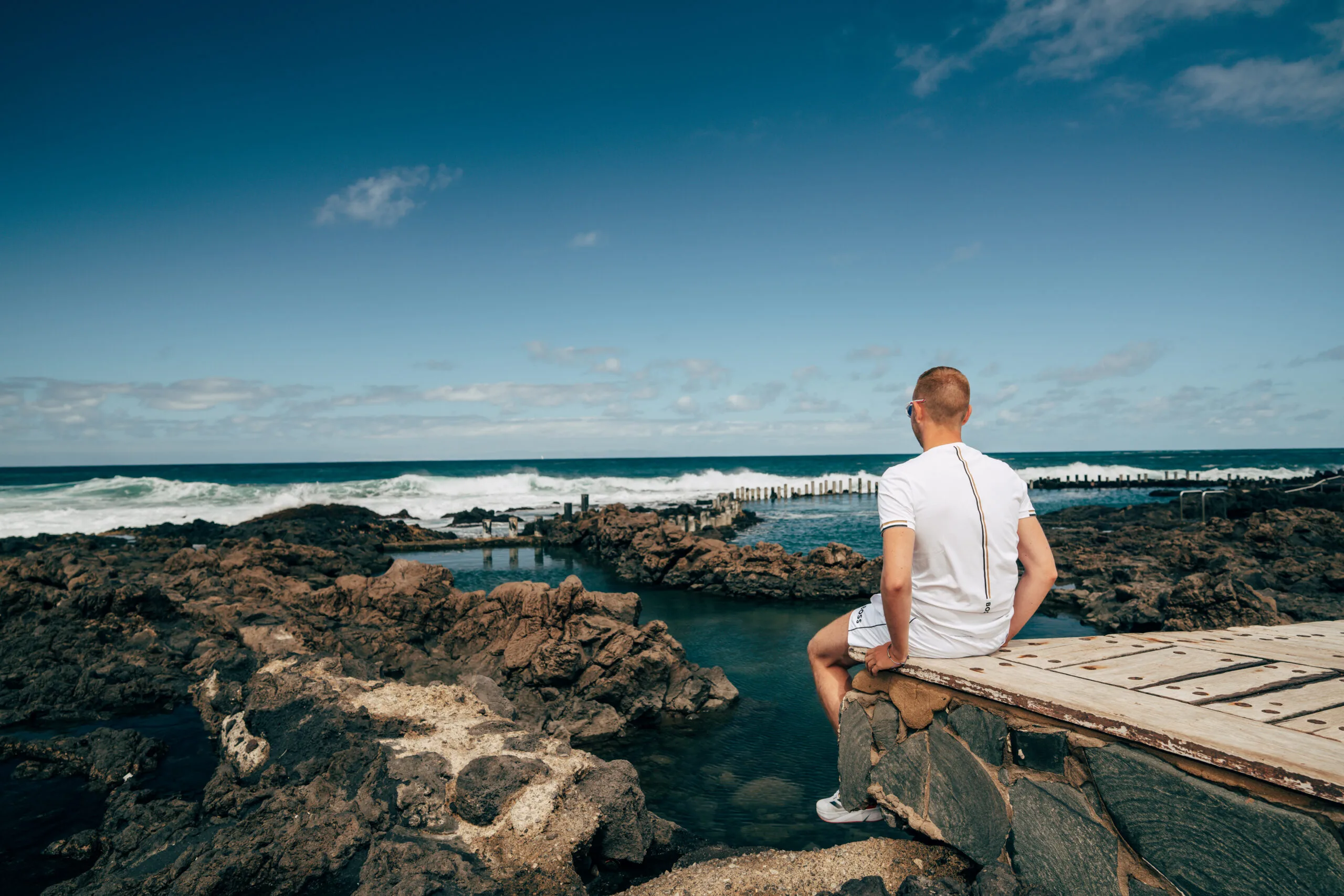 Man sitting on volcanic rock overlooking turquoise ocean natural pool Agaete Gran Canaria